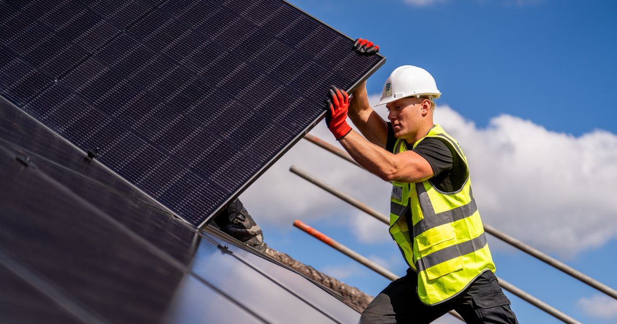 A Pro-Fit installer lifting an all-black solar panel into place on a tiled roof, mounting rails already run