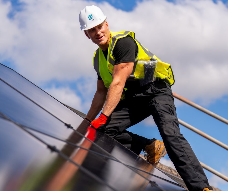 A Pro-Fit installer in a branded hard hat, hi-vis and work gloves stepping across a finished all-black solar array, one hand on a panel